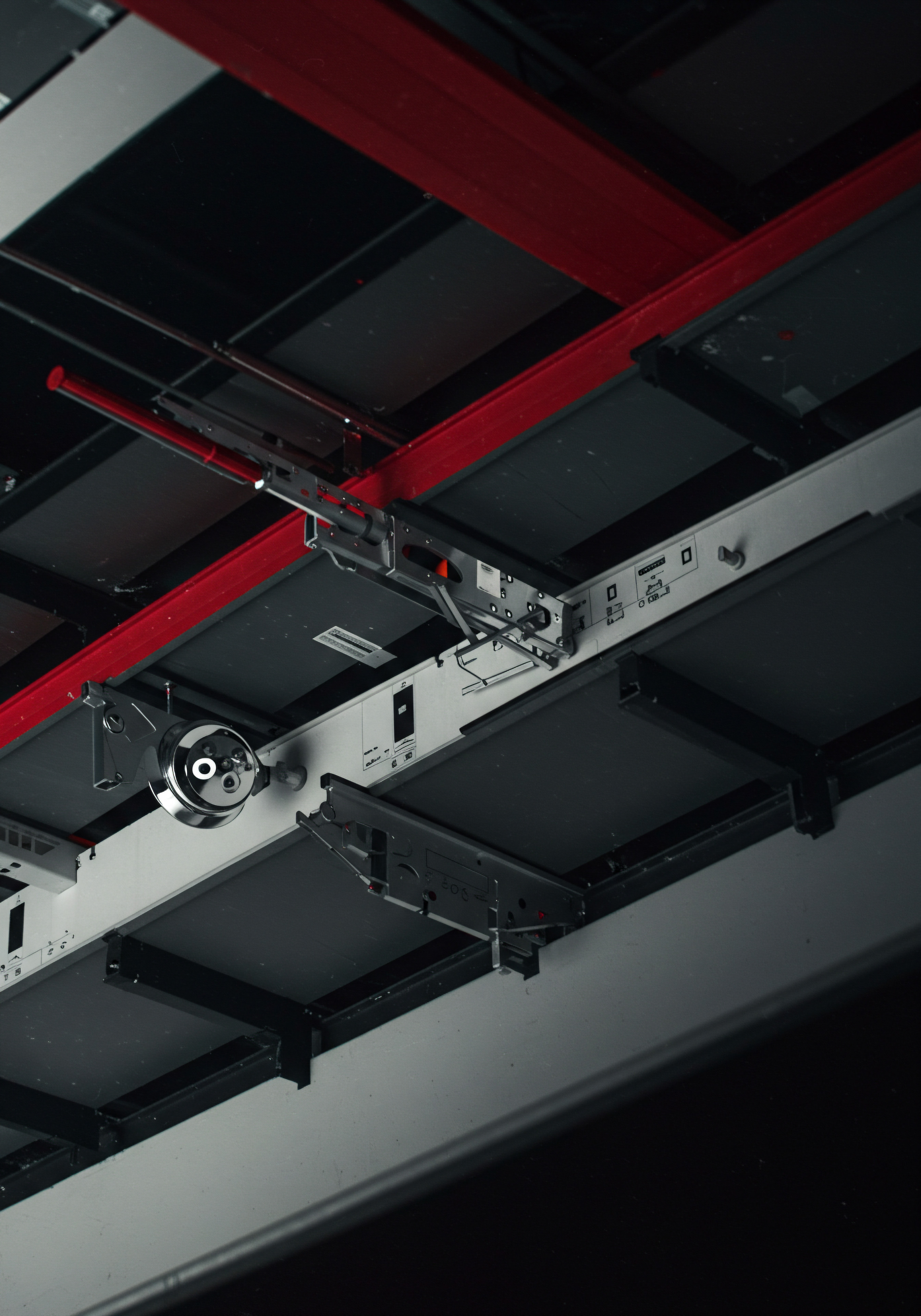Modern Office Ceiling SMB Business Automation Scaling Growth Strategy Implementation Viewed from an upward perspective, this office showcases a detailed overhead system of gray panels and supports with distinct red elements, hinting at a business culture focused on operational efficiency and technological innovation. The metallic fixture adds a layer of visual complexity and helps a startup grow to a scale up. The setup highlights modern strategies and innovative culture that SMB owners and their team must follow to improve productivity by planning a business strategy including automation implementation using various software solutions for digital transformation which helps in expansion and market share and revenue growth.