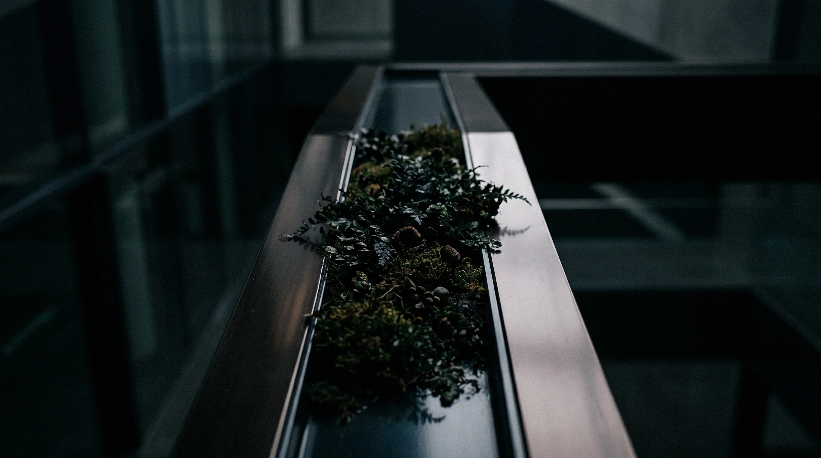 Moss and small plants fill the open channel of a metal rail above a glass floor.